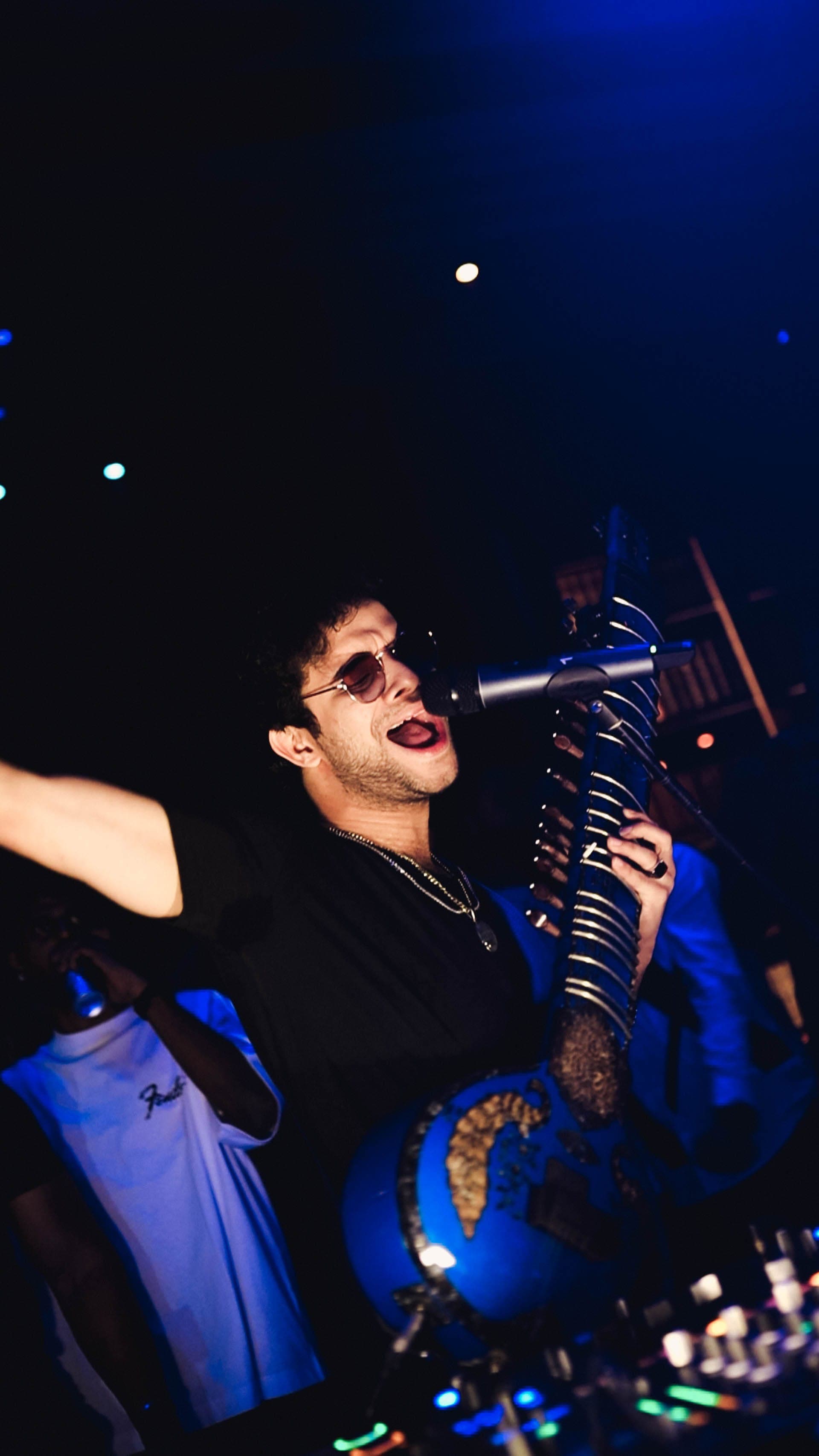 Akhlad Ahmed performing live, singing with sitar under blue stage light